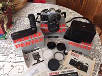 Wide view of Pentax Super Program camera with zoom lens attached, motor winder, flash, instruction manuals, lens caps, and original boxes on table.