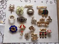Full spread of 17 assorted gold-toned brooches on white paper including animals, flowers, novelty and geometric designs.