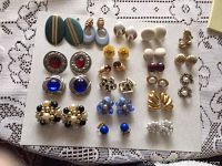 Top view of all 20 pairs of vintage clip-on earrings arranged on white paper showing various styles and colors including green, blue, yellow, red, cream, maroon, gold-tone and pearl accents.