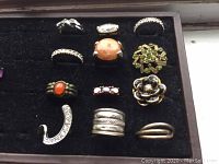 Close-up of 11 ladies rings displayed on black velvet. Shows tarnish on two sterling rings and details of costume rings with stones and designs.