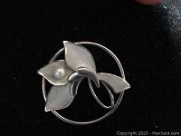 Front view of the sterling silver floral brooch with pearl accent against a dark background showing details of the shape and texture.