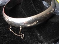 Close-up image showing the silver bangle bracelet with engraved patterns and attached safety chain.