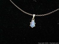 Close-up of the pendant showing the opal stone and gold setting on black background.