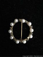 Front view of a circular brooch featuring pearls on a gold frame against a black background.