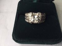 Front view of sterling silver ring with large clear center stone and smaller stones on the band in black display box.