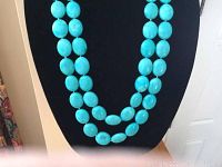 Front view of turquoise colored stone bead necklace displayed on black bust, showing double strand wear.