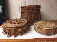 Photo showing all three baskets on a surface against a light wooden wall background, illustrating their shapes and relative sizes.