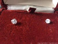 Pair of small stud earrings with clear stones set in yellow gold posts and butterfly backs, placed against red fabric to show details.