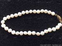 Full view of the pearl bracelet laid out with white pearls and a gold clasp.