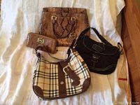 All four items laid out on white textile background: snakeskin tote, matching wallet, black Coach bag, plaid canvas hobo.