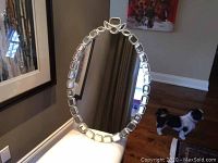 Full view of an oval mirror with an all-glass, geometric beveled segment frame on a table.