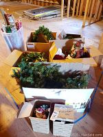 Boxes filled with assorted Christmas decorations including garlands and figurines seen from above in unfinished attic space