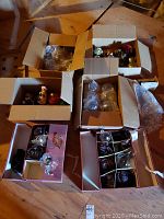 Overview photo of six open boxes filled with assorted ornaments made of glass and ceramic, placed on wooden floor in attic area