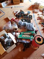 Photo shows multiple sets of Christmas string lights boxed and loose, assorted ornaments in plastic bags and boxes, and the red tin container of Wrap n Roll lights.