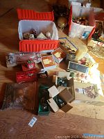 Photo showing several boxes, plastic bins, and loose holiday items including ornaments, candles, and decorative pine cones on a wooden floor.