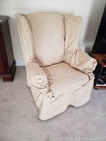 Full view of beige slipcovered armchair with visible wear and cat scratches on fabric