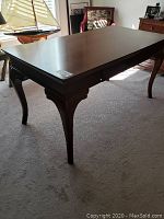 Full view of medium brown hardwood table with elegant cabriole legs on carpeted floor in living room setting.