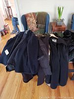 Various women's coats hanging on rack and chair including dark colored coats and fur-like material ones