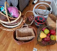 Overview of multiple wicker baskets of various shapes and sizes along with artificial fruit and decorative items, showing the quantity and variety of baskets.