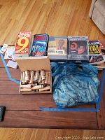 Overview photo showing paperback books by James Patterson and Patricia Cornwell, DVD covers, a box open with coin rolls, and a blue plastic bag containing additional items.
