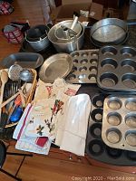 Full lot view showing all baking pans, utensils, towels, and chef hat arranged on a table.