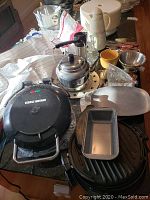 Full view of George Foreman grill with flat and ribbed surfaces, tea kettle, coffee carafe, colander, and yellow coffee cup on counter.