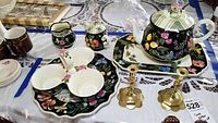 Full tea set displayed on table including teapot, creamer, sugar bowl, three-dish condiment set with serving plate, and two brass candlesticks.