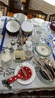 Full lot on table including Royal Albert soup bowls, Suzanne Nicole plates, Baum Polish teapot, two metal baskets with ceramic serving bowls, silverplate utensils, Corning Ware bakeware dishes.