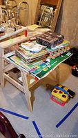 Photo showing Melissa and Doug wooden child's workbench covered with various books, art supplies and toys on a concrete floor with reflections and a mirror in background