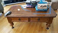 Front view of rectangular wooden coffee table with two drawers and items placed on top. Table shows some surface wear.