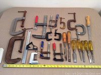Lot of assorted woodworking clamps and chisels laid out on fabric, shown with measuring tape for size reference.