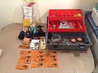 Wide view of the fishing tackle lot including reels, lures, hooks, and tackle box on a surface.