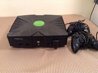 Full view of the original Xbox console and two controllers placed on a surface