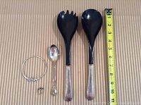 Silver Pandora bracelet, a small ornate spoon, a sterling silver ring, and serving tongs with black ends laid flat with measuring tape for scale