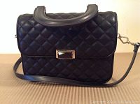 Front view of black quilted purse with gold-tone clasp and handle.