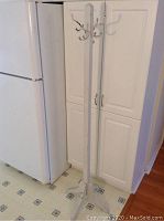 Full view of tall white painted antique hall tree standing near refrigerator and cabinet, showing overall shape and condition.