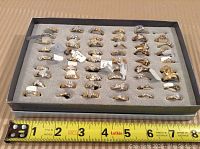 Tray of approximately 48 rings on grey foam with measuring tape for scale