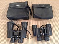 Both Bushnell binoculars with their respective cases, placed on a surface showing straps and overall condition.