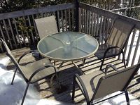 Full view of the metal framed patio table with glass top and four matching mesh fabric chairs on an outdoor wooden deck, snow visible on deck edges.