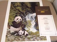 Print showing two giant pandas eating bamboo near a river, along with certificate of authenticity, on a white mat background.