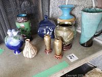 Nine assorted vases displayed on a table, showing various colors, shapes, and designs including the blue N and C Golden Century Italy vase and other decorative pieces.