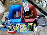 Wide shot showing two large plastic totes (blue and red) filled with assorted office supplies including calculators, staplers, and file holders.