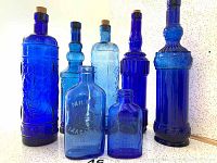 Full set of six blue handmade glass bottles, varying sizes and embossed designs, two smaller Milk of Magnesia bottles in front.