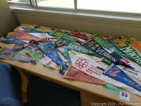 Overview of assorted vintage Canadian pennants displayed on a wooden desk under window light.