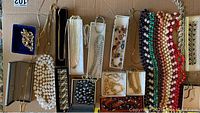 Top-down view of costume jewelry including pearl bracelets, chains, and beaded necklaces on brown surface