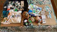 Multiple items displayed on bed including sweaters, plush mascots, pins, participation medals, and printed collectibles from 2010 Vancouver Winter Olympic Games.
