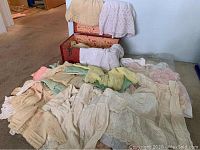 Full display of vintage 1960s infant and doll knitted sweaters, hats, dresses, laid out alongside opened red fabric covered box with floral lining