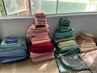Photo of assorted towels stacked by color near window, including blues, pink, green, red and neutral colors.