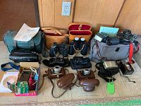 Photo showing entire lot including cameras, binoculars, recorder, cases, and accessories arranged on floor