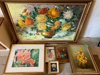 Wide shot showing six framed floral artworks grouped on floor and leaning against wall.